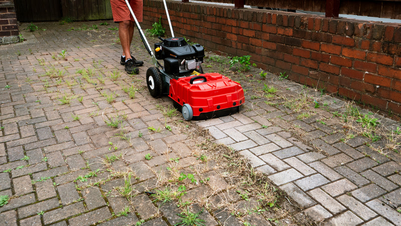 A person using a Weed Ripper on block paving, with weeds growing