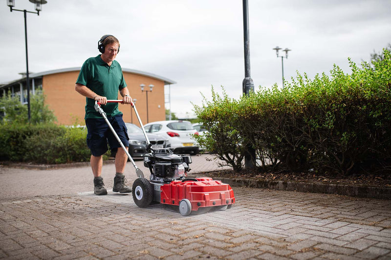 Person using a Westermann WKB430 Weed Ripper to clean block paving on a commercial site