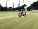 Person cleaning a tennis court with a Westermann WR870 Moss Brush with a double poly brush head