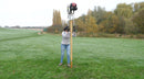 A person installing a tall post with the Easy Petrol Post Driver, with the Long Handles, in a countryside setting